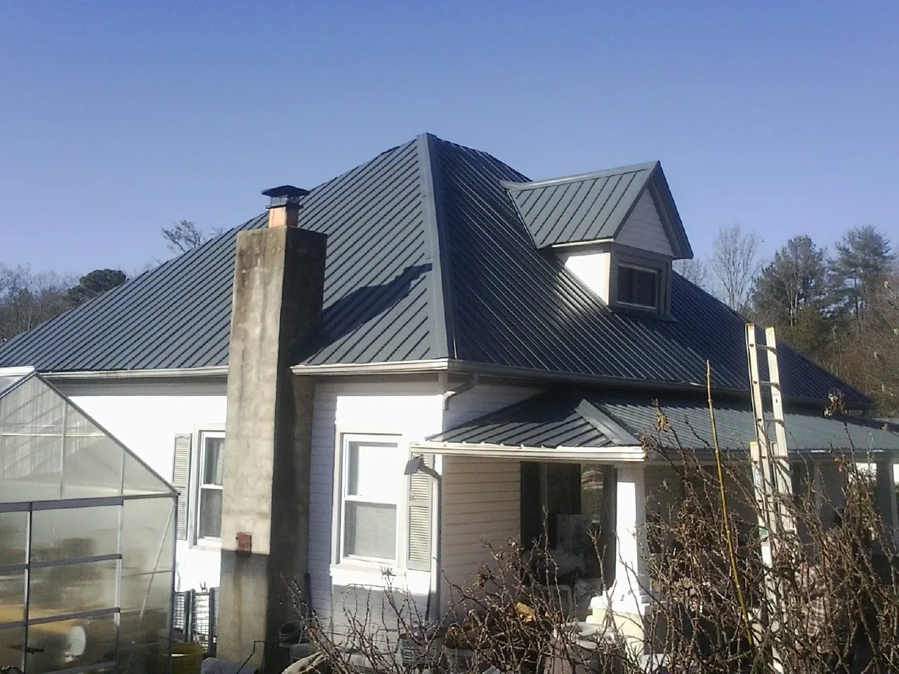 Dark blue standing seam metal roof on a white farmhouse with dormer — Slate & Tile Roof Repair by Roofing Brothers in Middle Island