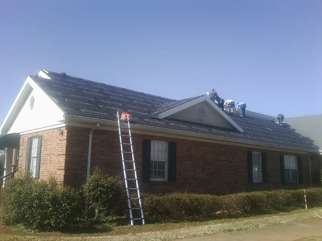 Crew tearing shingles off a brick ranch roof with a ladder set — Emergency Roof Repair work by our crew in Middle Island