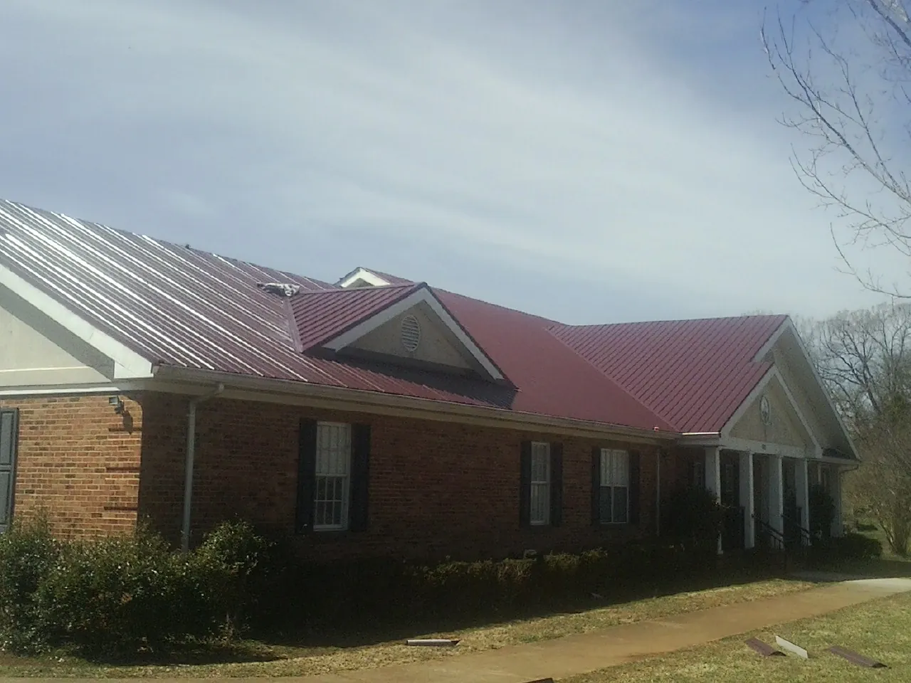 Red metal roof with gabled entries on a long brick building, from a Hail Damage Roof Repair job in Middle Island