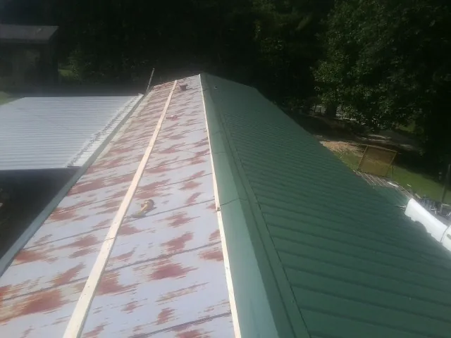 Old rusted panels beside newly installed green metal roofing — Wind Damage Roof Repair by Roofing Brothers in Middle Island