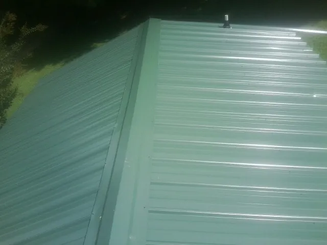 New green metal panels meeting at the ridge of a roof — Flat Roof Repair work by our crew in Middle Island