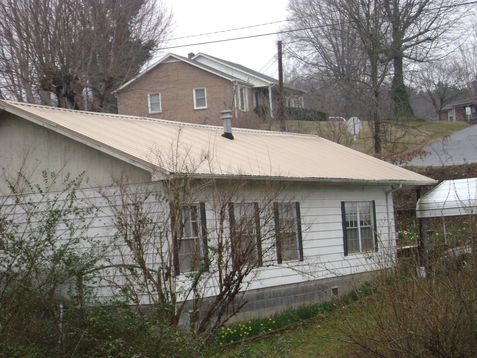 Tan metal roof on a white sided house set into a hillside — Commercial Roofing by Roofing Brothers in Middle Island