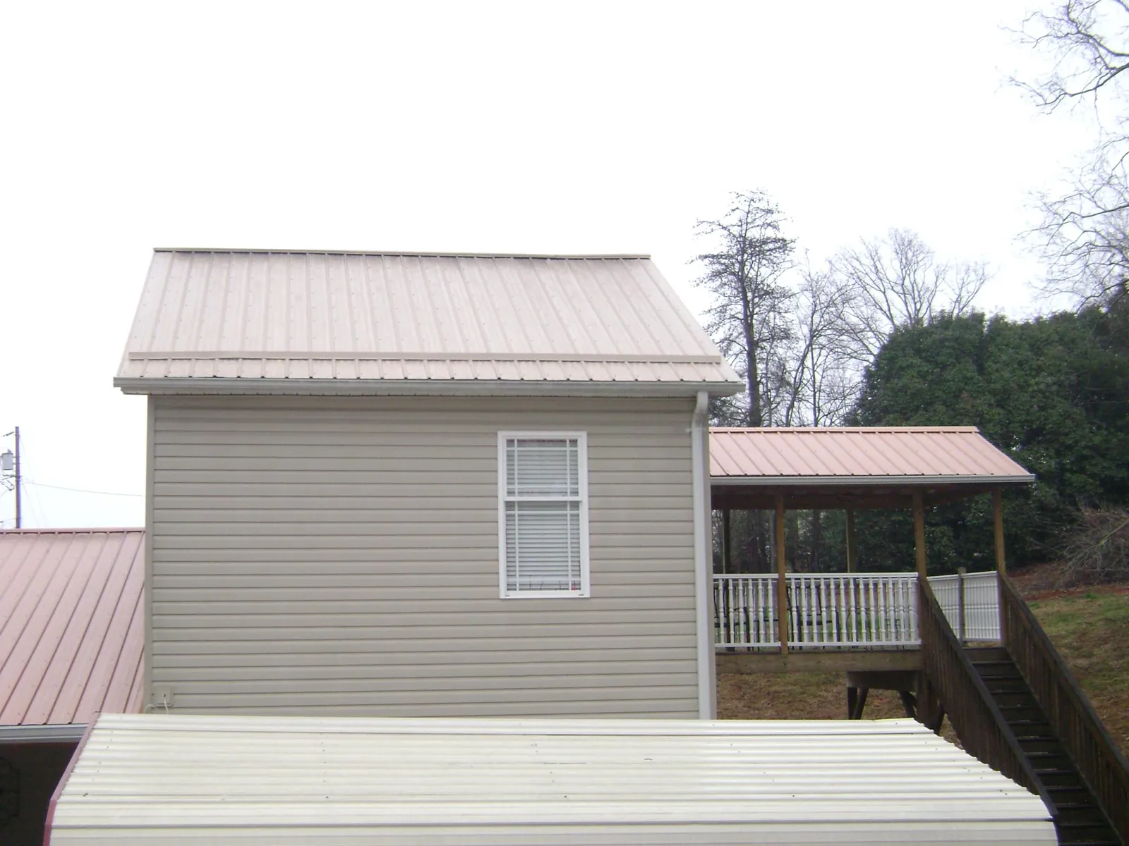 Tan metal roofs on a two story addition and attached porch, from a Roof Replacement job in Middle Island